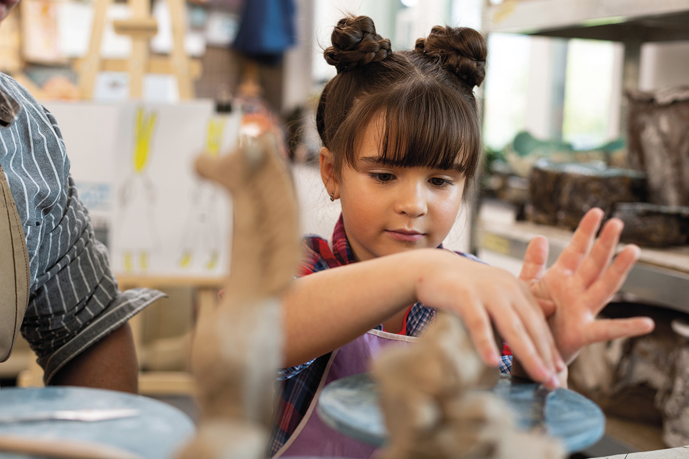 Using hands. Dark-eyed schoolgirl with nice hairstyle using her hands while sculpting clay figures